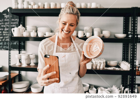 Hey, look guys. Cropped shot of an attractive mature woman using her cellphone to take a selfie with her pottery in her studio. 92891649