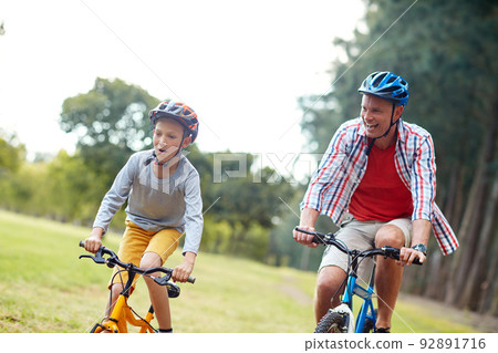 They love racing each other. Shot of a father and son riding bicycles in a park. They love racing each other. Shot of a father and son riding bicycles in a park. 92891716