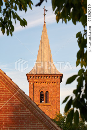 Low angle of a church bell tower against a blue sky. Exterior view of a traditional old religious red brick building on a sunny day. Wall and roof of an historic house or home architecture design Low angle of a church bell tower against a blue sky. Exterior view of a traditional old religious red brick building on a sunny day. Wall and roof of an historic house or home architecture design 92892019