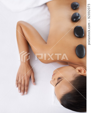 Step one to total relaxation. Shot o a young woman getting a hot rock treatment at a spa. 92892073