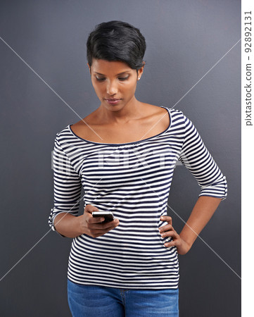 Sending a text. Studio shot of a beautiful young woman sending a text message against a grey background. Sending a text. Studio shot of a beautiful young woman sending a text message against a grey background. 92892131