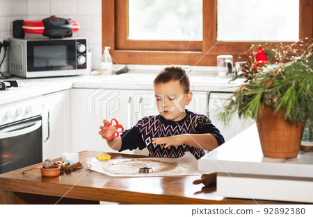 A boy prepares gingerbread cookies in the kitchen. Christmas family traditions. Leisure of the child during the New Year holidays. A boy prepares gingerbread cookies in the kitchen. Christmas family traditions. Leisure of the child during the New Year holidays. 92892380