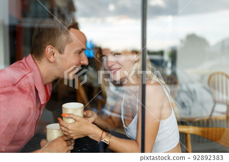 Romantic loving couple drinking coffee, having a date in the cafe, view through window. 92892383