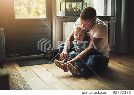 Getting ready for a day out. Shot of a father helping his son put on his shoes at home. 92892386