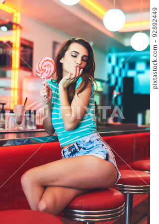 Something sweet.... Cropped shot of an attractive young woman eating a giant lollipop in a retro diner. 92892449