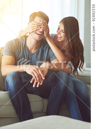 Ive got a surprise for you. A young woman covering her husbands eyes for a surprise. 92892550