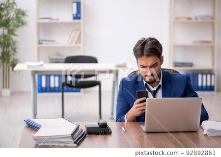 Young male employee unhappy with excessive work in the office Young male employee unhappy with excessive work in the office 92892861