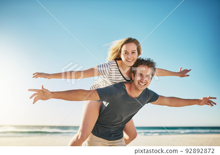 Love makes us feel alive. Shot of a happy young couple enjoying a piggyback ride at the beach. 92892872
