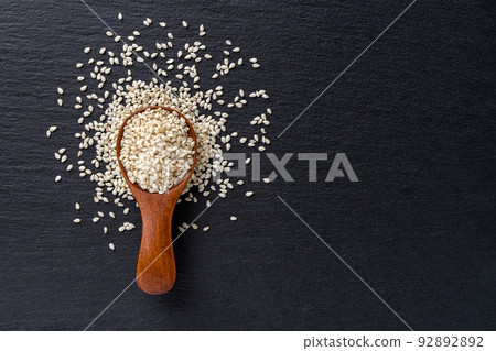 Raw sesame seeds in a wooden spoon over black slate background. 92892892