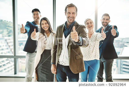 They only work towards success. Portrait of a group of cheerful businesspeople standing together while showing thumbs up to the camera inside of the office. They only work towards success. Portrait of a group of cheerful businesspeople standing together while showing thumbs up to the camera inside of the office. 92892964
