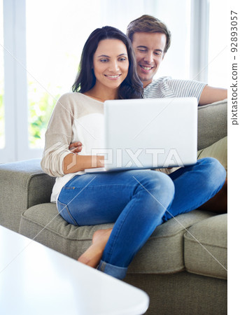 Browsing together. A young couple using their laptop while sitting on the sofa at home. Browsing together. A young couple using their laptop while sitting on the sofa at home. 92893057
