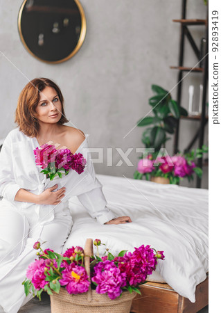 a beautiful woman in white clothes with a peonies in the bedroom. home comfort. 92893419