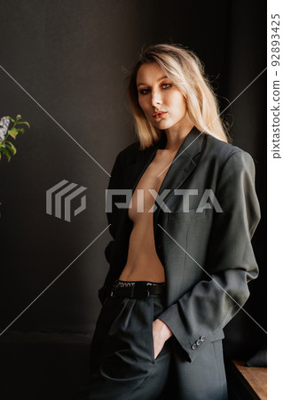 a sexy and slender blonde woman in a black jacket on a naked body in a dark room 92893425