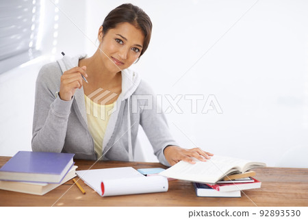 Hitting the books with a positive attitude. A pretty young university student studying for her finals in her dorm room. Hitting the books with a positive attitude. A pretty young university student studying for her finals in her dorm room. 92893530