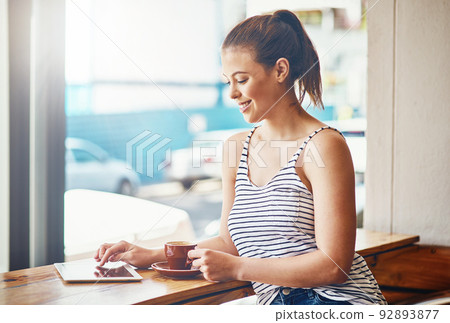 Coffee and wifi - the best way to spend the day. Shot of a young woman using her digital tablet in a coffee shop. Coffee and wifi - the best way to spend the day. Shot of a young woman using her digital tablet in a coffee shop. 92893877