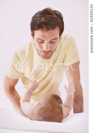 He treasures moments like these with his daughter. A father showing affection to his baby daughter as she lies on a changing table. 92894120
