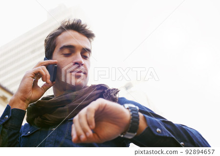 Hes always got some time..... Low angle shot of a man chekcing his watch while talking on his cellphone. 92894657