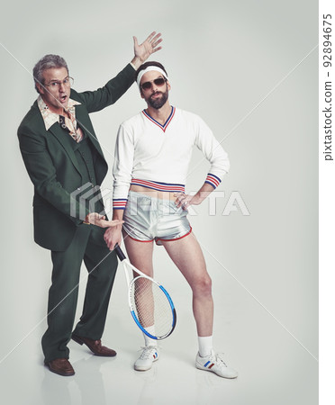 Agent pushing his new tallent. A mature man in a retro suit trying to present a young man in retro tennis clothes. 92894675