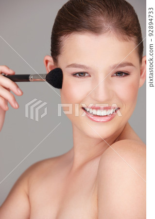 Just a light blush.... Studio shot of a beautiful woman applying blush to her cheeks. 92894733