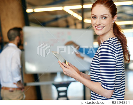 Just another day in the office...works going great. Shot of a young businesswoman holding a digital tablet with her colleagues in the background. Just another day in the office...works going great. Shot of a young businesswoman holding a digital tablet with her colleagues in the background. 92894854