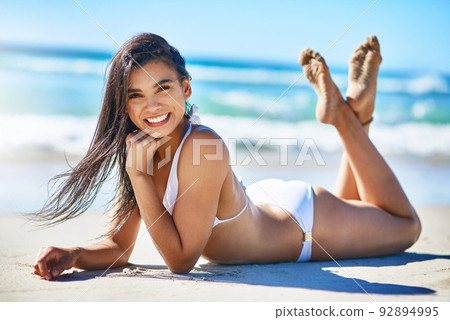 Lapping up the rays at the beach. Portrait of a beautiful young woman in a white bikini posing on the beach. 92894995