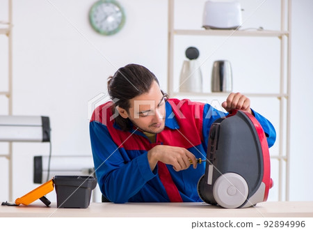 Young male contractor repairing vacuum cleaner at workshop Young male contractor repairing vacuum cleaner at workshop 92894996