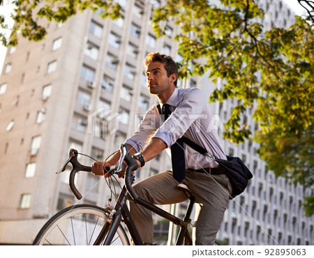 Off to work on his wheels. Shot of a businessman commuting to work with his bicycle. 92895063