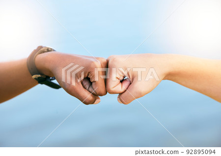Female friends feeling supported, united and touching fists at the knuckles. Feeling motivated and ready to achieve. Closeup of two unknown people giving each other a fist bump against blue copyspac Female friends feeling supported, united and touching fists at the knuckles. Feeling motivated and ready to achieve. Closeup of two unknown people giving each other a fist bump against blue copyspac 92895094
