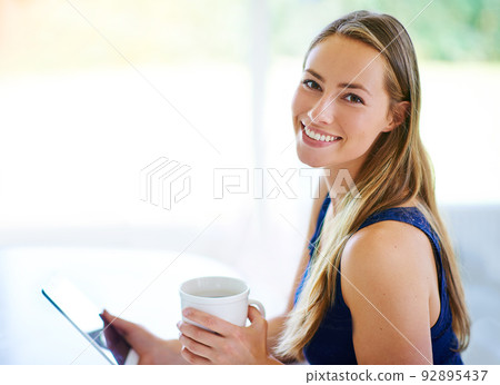I have all the company I need right here..... Shot of a young woman using her digital tablet while having cup of coffee. 92895437