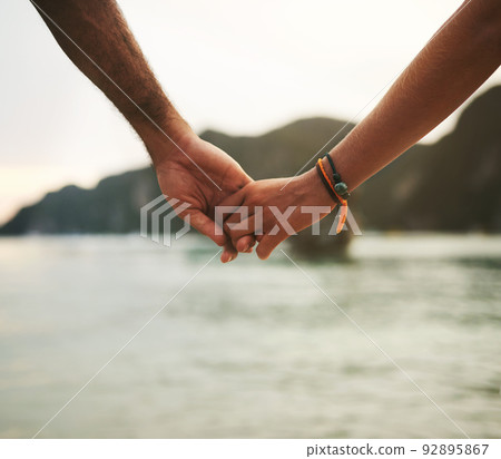 Explore the world with the one you love. Closeup shot of a young couple holding hands at the beach. 92895867