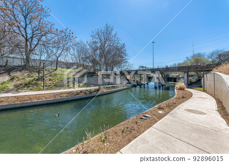 Small river with concrete walkways on the side heading to a bridge at San Antonio, Texas Small river with concrete walkways on the side heading to a bridge at San Antonio, Texas 92896015
