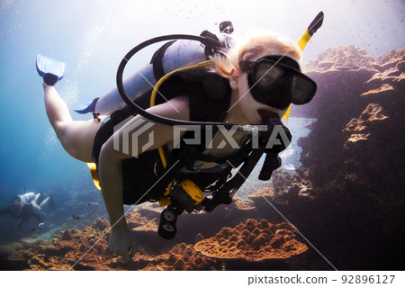 Ocean adventurer. Female scuba diver closely passes over a coral reef. 92896127