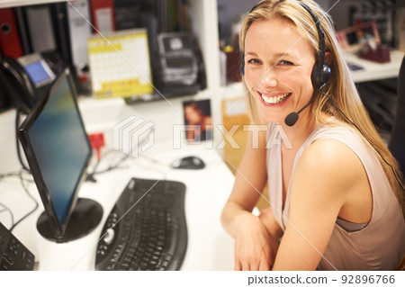 How can I assist. Cropped portrait of a smiling businesswoman wearing a headset at her desk. How can I assist. Cropped portrait of a smiling businesswoman wearing a headset at her desk. 92896766