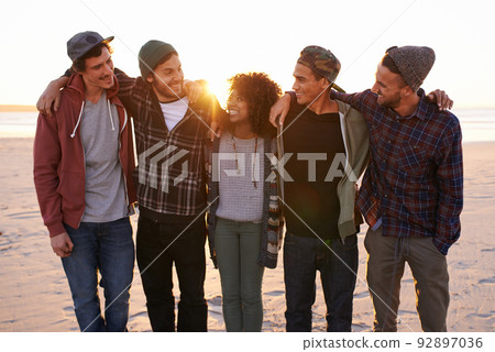 Friends make the world a better place. Shot of a group of friends walking along a beach at sunset. 92897036