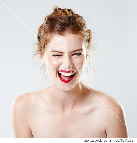 When in doubt... wear red. Studio shot of a beautiful young woman with bare shoulders winking at the camera. 92897132