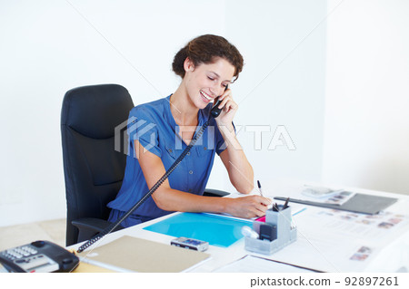 Shes hard at work. Shot of a businesswoman talking on the phone while working at her office desk. Shes hard at work. Shot of a businesswoman talking on the phone while working at her office desk. 92897261