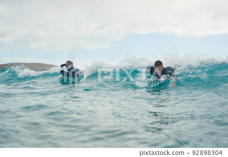 Surfing allows us to feel at one with nature. Shot of a young couple out surfing together at the beach. Surfing allows us to feel at one with nature. Shot of a young couple out surfing together at the beach. 92898304