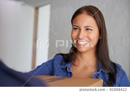 Excited to get settled in. A beautiful young woman smiling at the camera as she takes a box from a mover. Excited to get settled in. A beautiful young woman smiling at the camera as she takes a box from a mover. 92898422