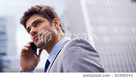 A smart phone for a savvy businessman. A low angle shot of a handsome young businessman using his cellphone in the city. 92898543