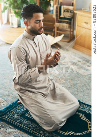 Prayer is devotion. Shot of a young muslim man praying in the lounge at home. 92898622