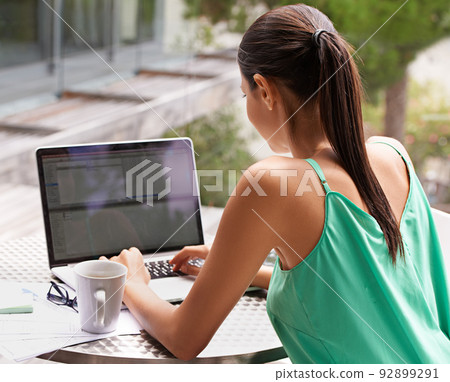 She makes technology work for her. Rearview shot of a young woman working on her laptop outside. She makes technology work for her. Rearview shot of a young woman working on her laptop outside. 92899291
