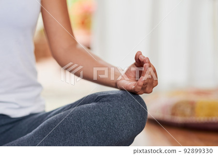 Finding your inner peace. Shot of an unrecognizable woman doing a yoga pose with her legs grossed and seated on the ground at home. Finding your inner peace. Shot of an unrecognizable woman doing a yoga pose with her legs grossed and seated on the ground at home. 92899330