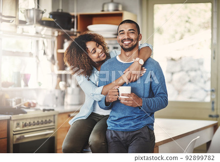 Happy, hugging and smiling young in love couple bonding in a kitchen at home. Romantic life partners enjoying the morning together feeling relaxed and loving. Portrait of a people embracing romance 92899782