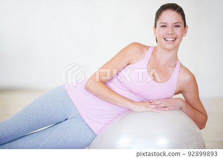 Feeling positive about her fitness goals. Portrait of a young woman leaning on an exercise ball. Feeling positive about her fitness goals. Portrait of a young woman leaning on an exercise ball. 92899893