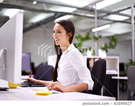 Enjoying every minute of work. Cropped shot of an attractive young woman working at her desk. Enjoying every minute of work. Cropped shot of an attractive young woman working at her desk. 92899927