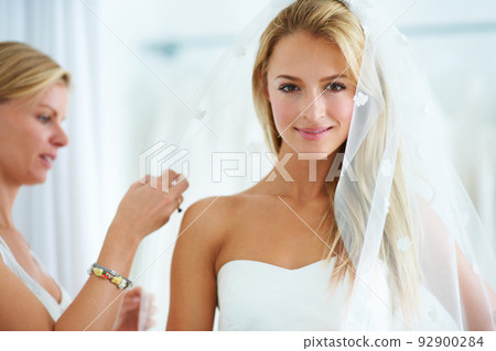 Putting on the final touches. A young woman trying on wedding dresses in a bridal boutique. Putting on the final touches. A young woman trying on wedding dresses in a bridal boutique. 92900284