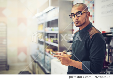 Social media plays a serious role in advertising. Shot of a man using his cellphone while standing in a coffee shop. 92900622