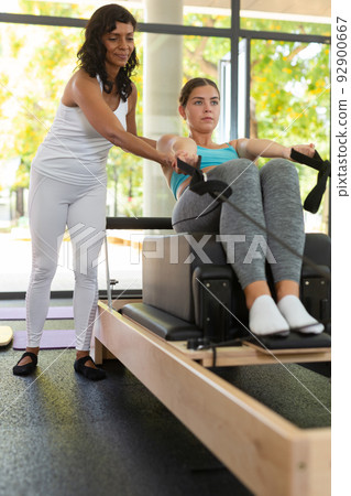 Woman pilates trainer helping young woman with reformer exercises Woman pilates trainer helping young woman with reformer exercises 92900667