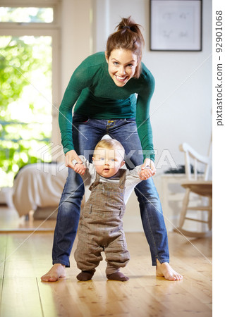 Hes learning so fast. Smiling young mom helping her baby boy learn to walk. Hes learning so fast. Smiling young mom helping her baby boy learn to walk. 92901068