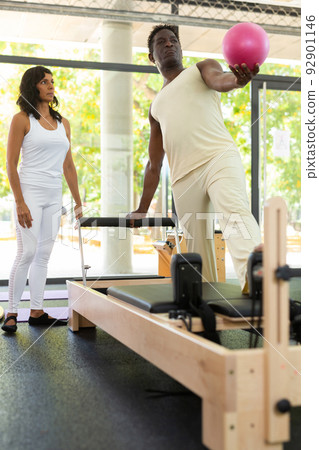 Man exercising pilates with female trainer in gym Man exercising pilates with female trainer in gym 92901146